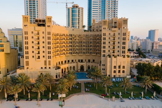 Aerial view of a luxury hotel in Ajman city surrounded by palm trees and urban landscape.