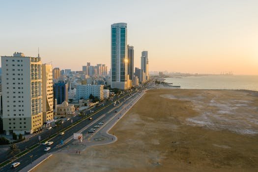 Aerial view of a coastal city with skyscrapers, streets, and sea at sunset, showcasing urban life.